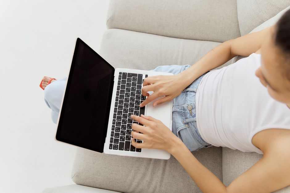Professional property host sits in a bright, modern living room, thoughtfully typing on a laptop to communicate with a guest.