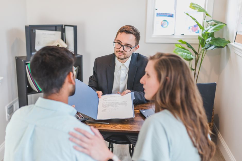 A couple sits at a bright dining table, thoughtfully reviewing paperwork with a laptop, symbolizing the financial decision-making process of selling a home.