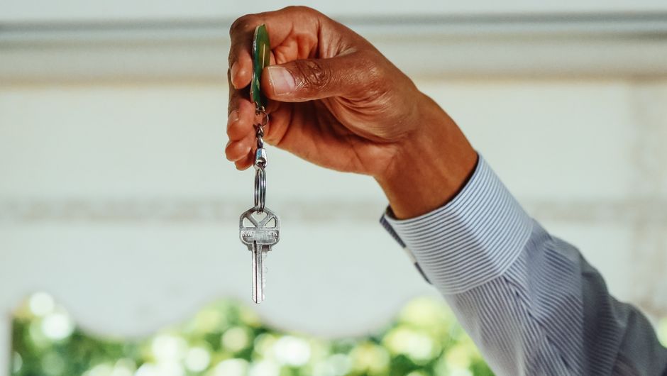 A professional real estate agent hands over keys to a client in front of a modern home, representing a successful and transparent property sale.